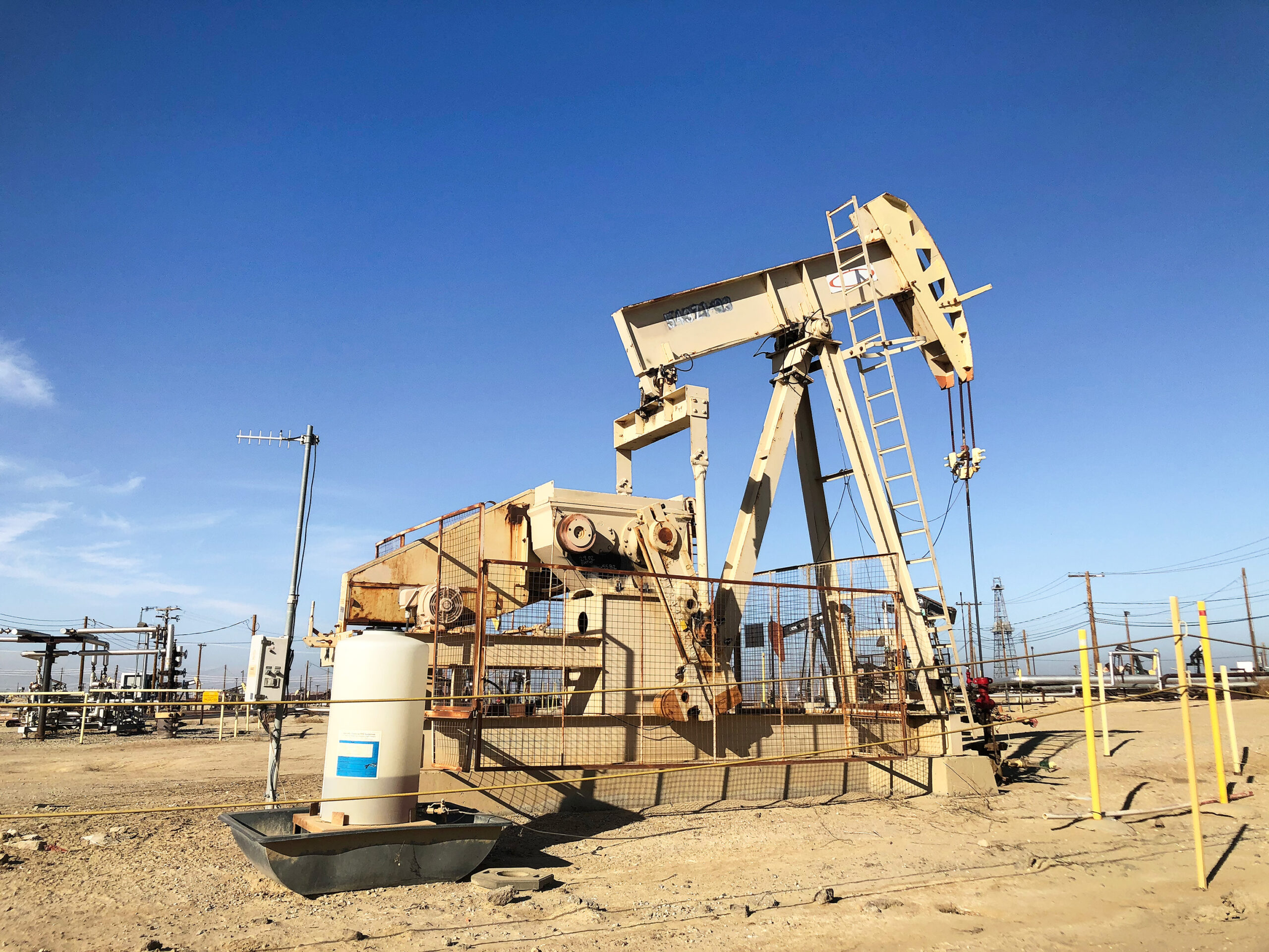 A pump-jack in a desert near power lines.