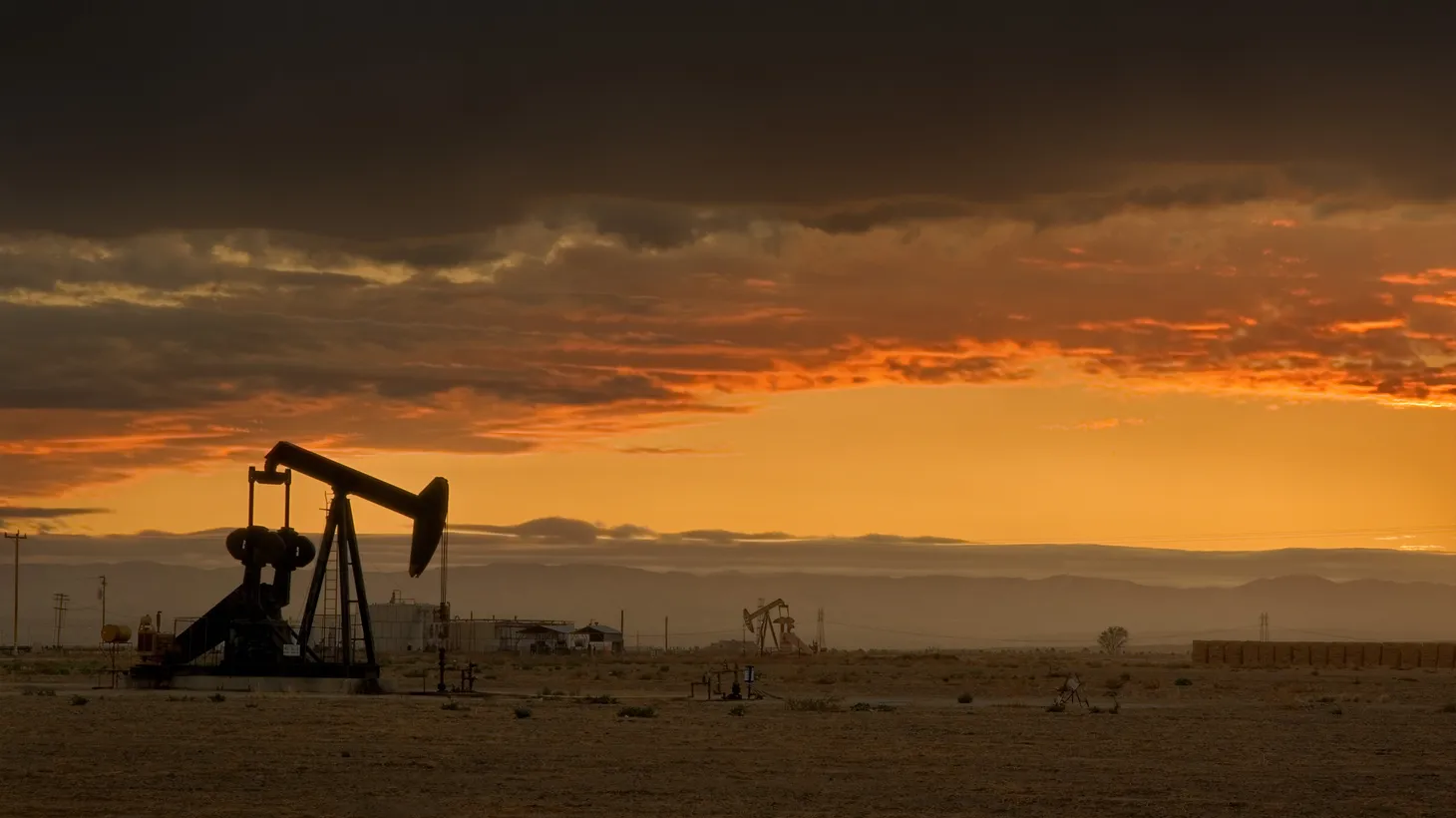 The sun setting over the San Joaquin Valley in Central California. In the foreground is an oil pumpjack.